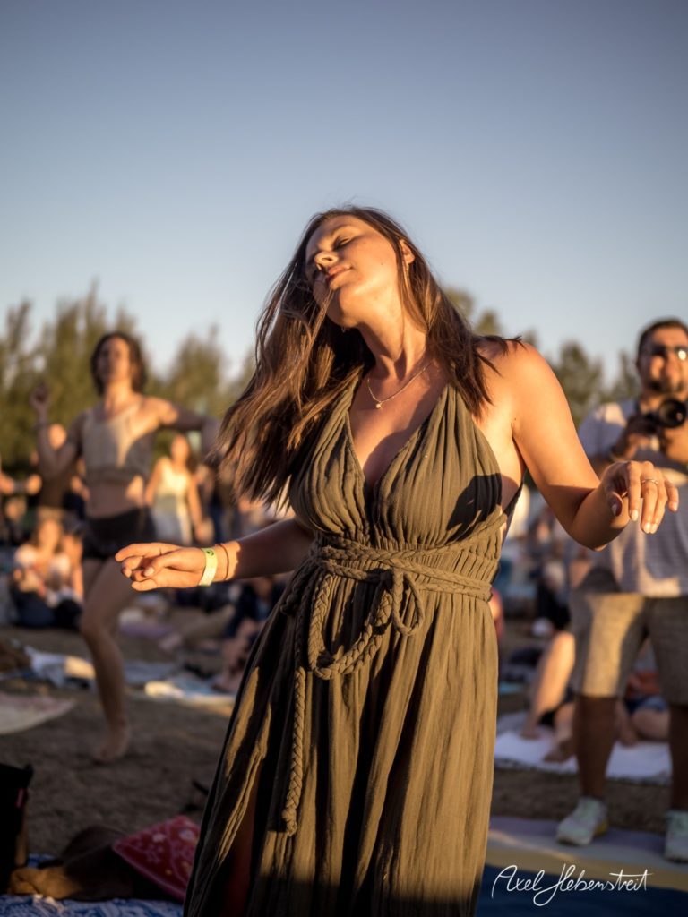 Frau in einem fließenden Kleid tanzt ausgelassen bei Sonnenuntergang auf einem Festival – © Axel Hebenstreit