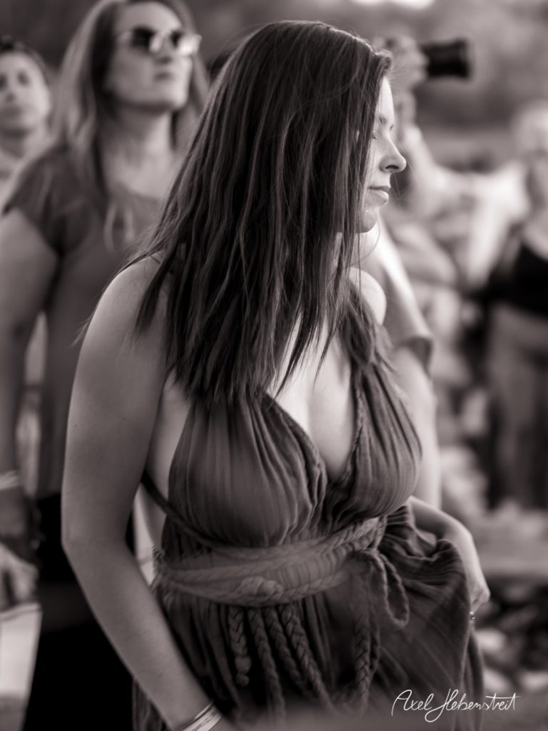 Eine nachdenklich wirkende Frau in einem eleganten Kleid, umgeben von Festivalbesuchern in einer lebhaften Atmosphäre – © Axel Hebenstreit