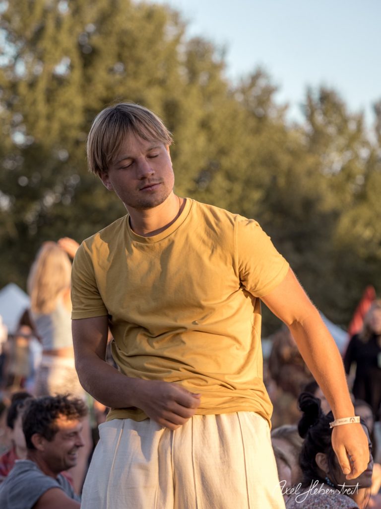 Junger Mann in gelbem T-Shirt tanzt entspannt auf einem Festival im Freien – © Axel Hebenstreit