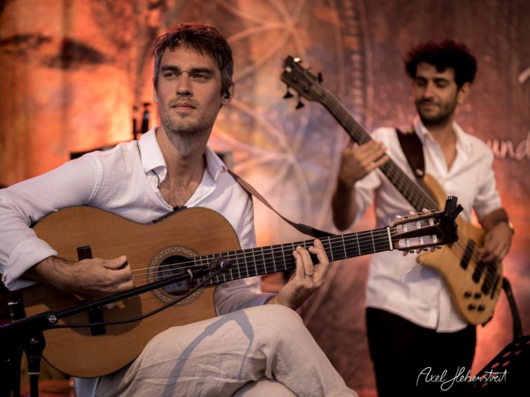 Ein Musiker spielt konzentriert auf einer akustischen Gitarre, während ein Bassist im Hintergrund begleitet – © Axel Hebenstreit