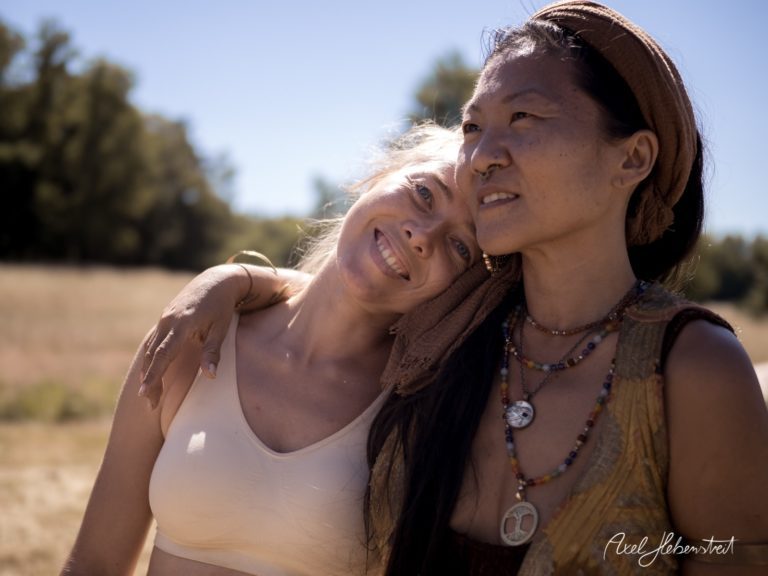 Zwei Frauen umarmen sich lächelnd in einer sonnigen Naturkulisse. – © Axel Hebenstreit