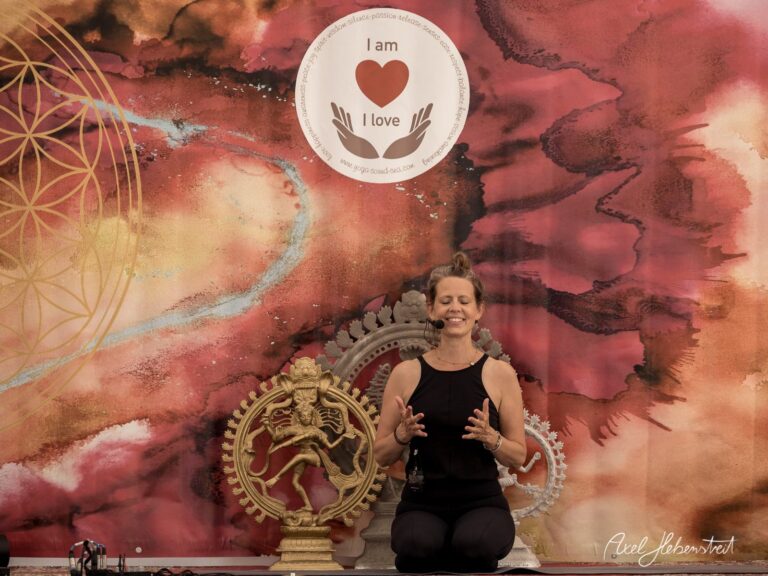 Frau in meditativer Pose vor einem kunstvoll gestalteten Hintergrund, der eine liebevolle Stimmung ausstrahlt – © Axel Hebenstreit
