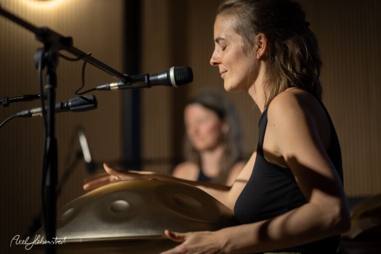 Musikerin spielt Hang-Trommel bei intimer Live-Performance mit Mikrofon und warmem Bühnenlicht