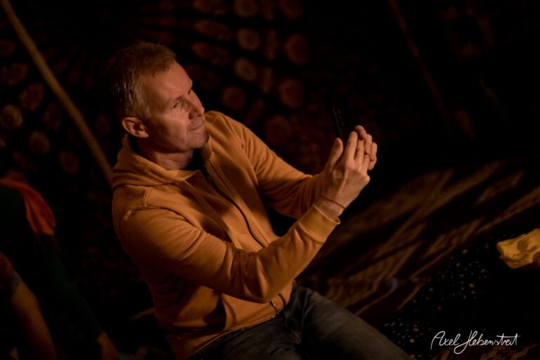 Ein Mann in einem oranges Sweatshirt fotografiert in einem stimmungsvollen, gedämpften Raum. – © Axel Hebenstreit