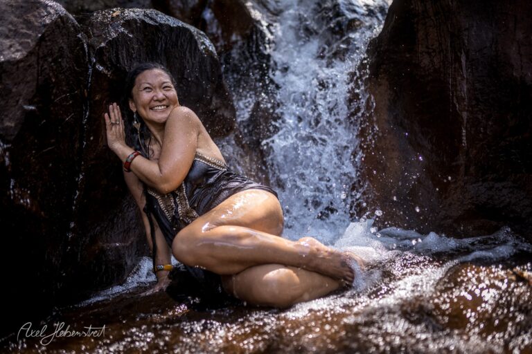 Eine lächelnde Frau genießt das Wasserfall-Erlebnis in der Natur und posiert vergnügt im Wasser – © Axel Hebenstreit