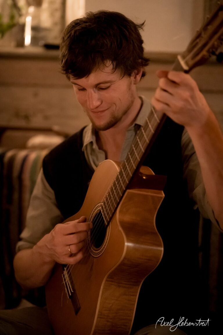 Ein junger Mann spielt konzentriert Gitarre in einer gemütlichen, rustikalen Umgebung – © Axel Hebenstreit