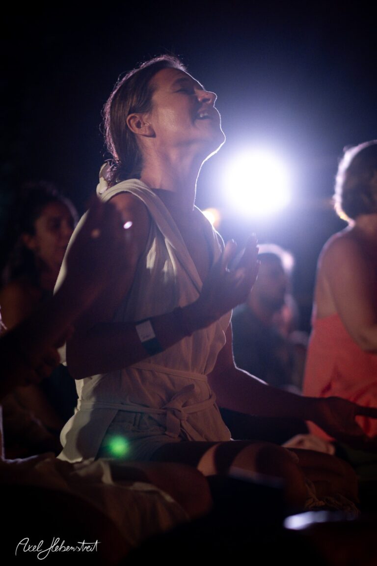 Eine Teilnehmerin in einer meditativen Pose bei einem Festival unter dem mystischen Licht. – © Axel Hebenstreit