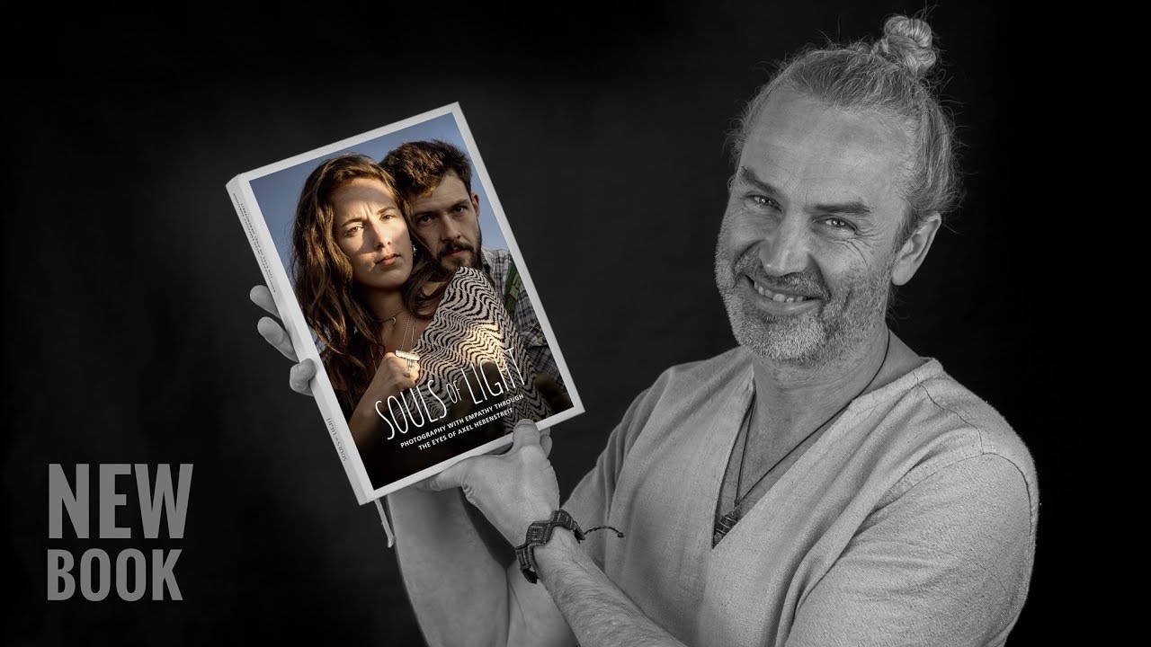 Ein lächelnder Mann präsentiert stolz sein neues Buch mit einem dramatischen Cover im Hintergrund. – © Axel Hebenstreit
