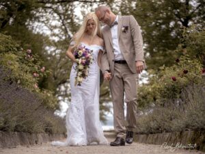 Braut und Bräutigam gehen Hand in Hand durch einen romantischen Garten – © Axel Hebenstreit
