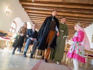 Eine Braut und ein Bräutigam in traditioneller Tracht schreiten in die Kirche, umgeben von Gästen in festlicher Stimmung. – © Axel Hebenstreit