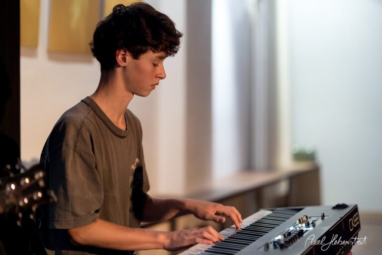 Junger Musiker spielt konzentriert auf einem E-Piano während eines Konzerts in einer modernen Umgebung – © Axel Hebenstreit